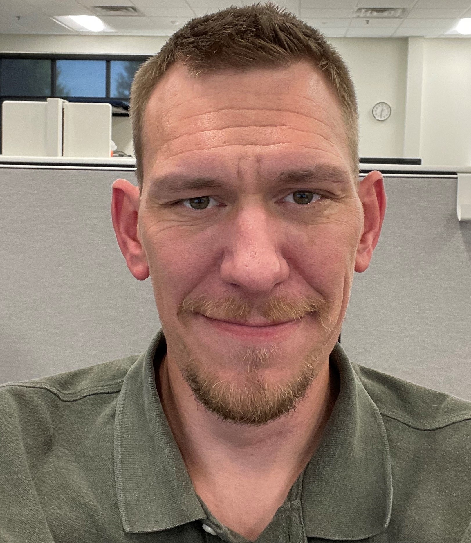 A headshot of a male with short, light brown hair and light colored skin, with slight facial hair, wearing a green colored polo shirt. 