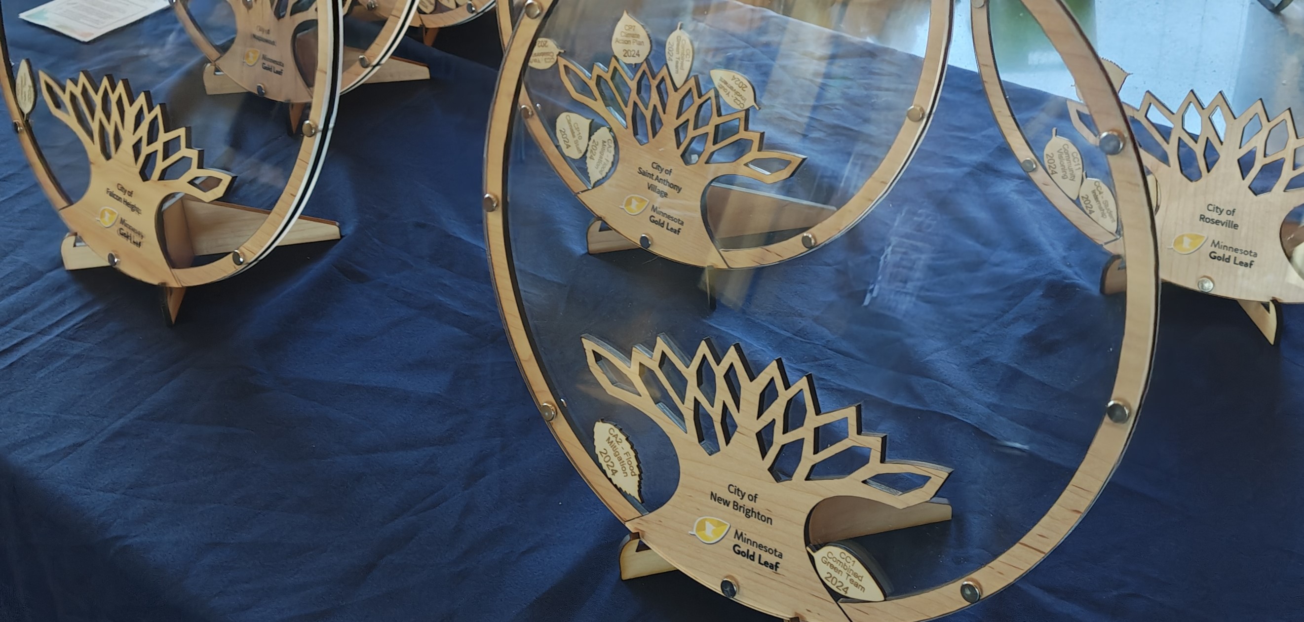 Gold Leaf awards displayed on a table. Acrylic circle with a tree trunk and branches. Leaves added to the branches with award name and year